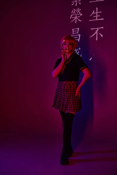 Donna sorridente in uniforme scolastica in luce al neon su sfondo viola con geroglifici, cosplayer — Foto stock