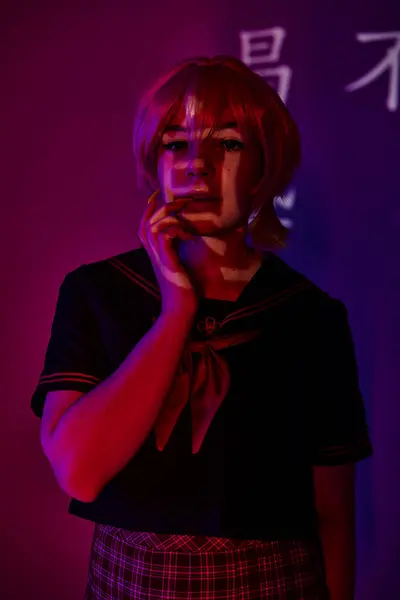 Portrait of dreamy anime woman in school uniform in neon light on purple backdrop with hieroglyphs — Stock Photo