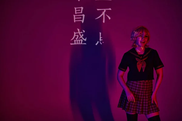 Anime donna in uniforme scolastica sporgente lingua in luce al neon su sfondo viola con geroglifici — Foto stock