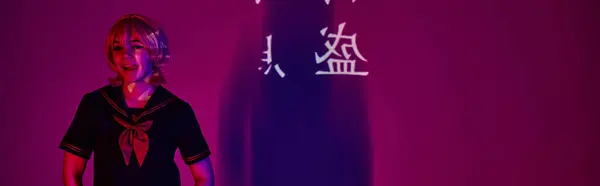 Косплей жінка в шкільній формі стирчить язиком в неоновому світлі на фіолетовому з ієрогліфами, банер — стокове фото