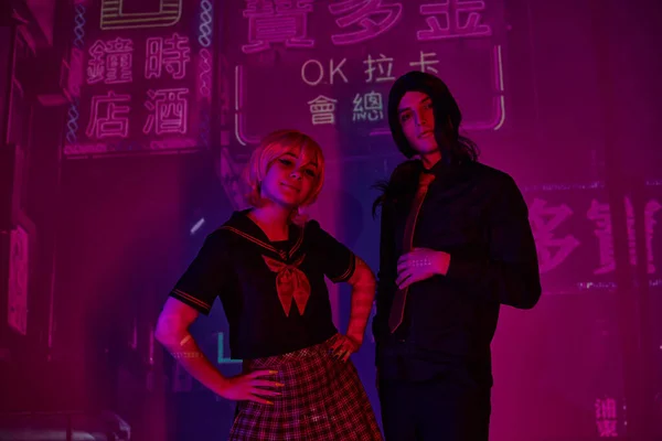 Anime donna con le mani sui fianchi vicino uomo alla moda in luce al neon su sfondo viola con geroglifici — Foto stock