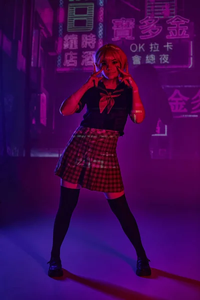 Anime model in school uniform showing victory signs on purple neon backdrop with hieroglyphs — Stock Photo