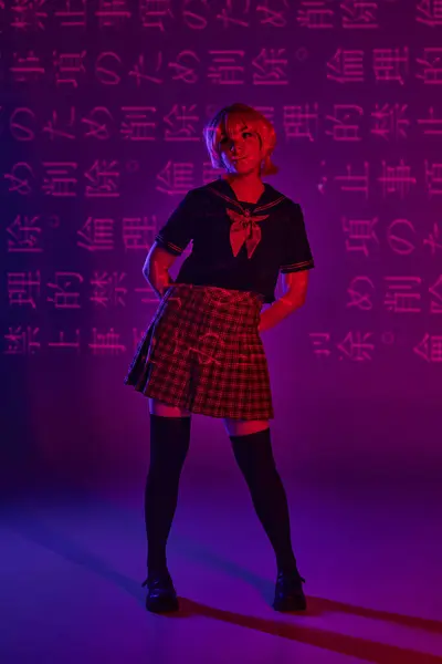 Молода жінка позує в шкільній формі на неоновому фіолетовому тлі з ієрогліфами, стиль аніме — стокове фото