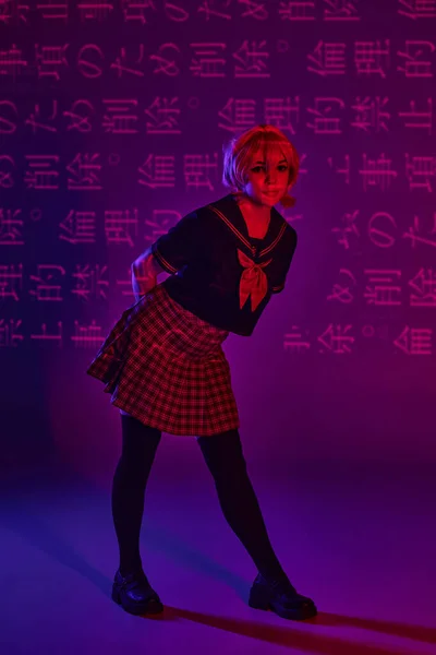 Pretty woman in school uniform posing on neon purple backdrop with hieroglyphs, anime trend — Stock Photo