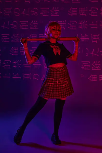 Молода аніме жінка в шкільній формі з бейсбольною битою на неоновому фіолетовому фоні з ієрогліфами — стокове фото