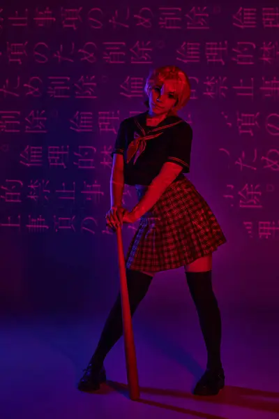 Сучасна аніме жінка в шкільній формі з бейсбольною битою на неоновому фіолетовому фоні з ієрогліфами — стокове фото