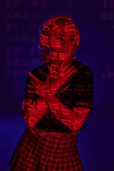 Женщина в стиле аниме со скрещенными руками, смотрящая в неоновую проекцию иероглифов на голубом фоне — стоковое фото