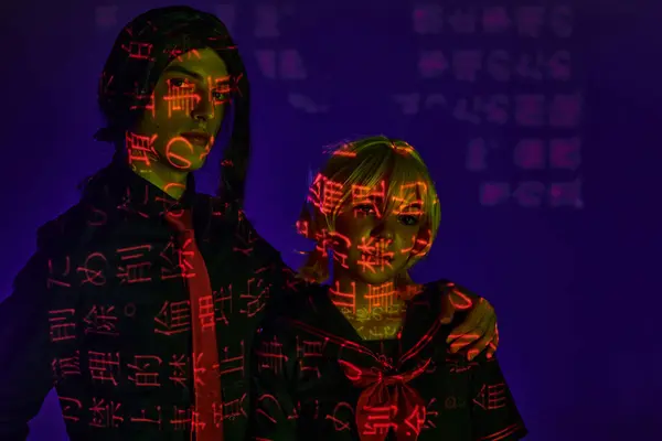 Cosplay students in colorful neon projection of hieroglyphs on blue indigo backdrop in studio — Stock Photo