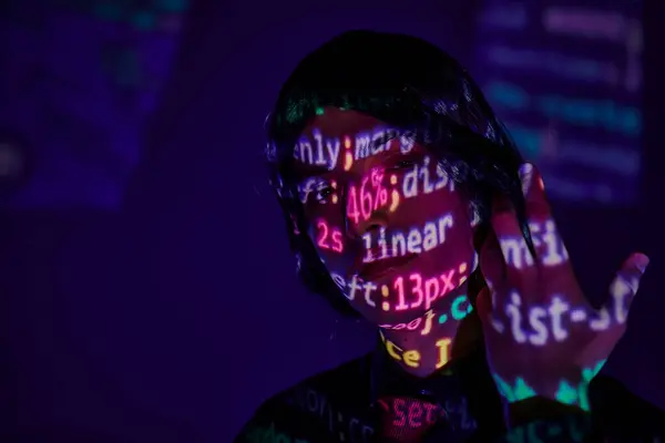 Anime style student in black wig in neon light with programming symbols on dark blue backdrop — Stock Photo