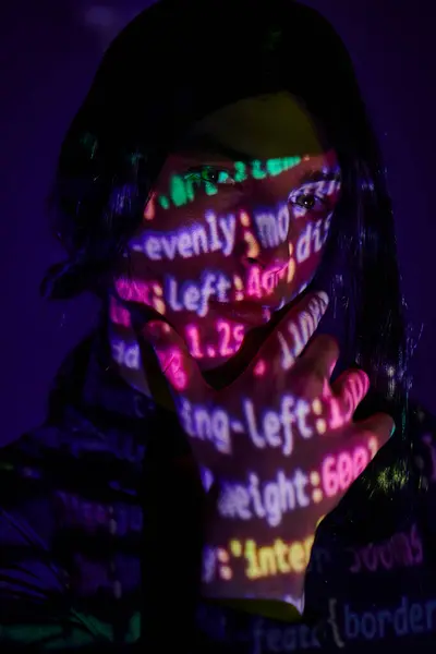 Student im Anime-Stil blickt in Neonlicht auf Kamera mit Programmiersymbolen auf dunkelblau — Stockfoto