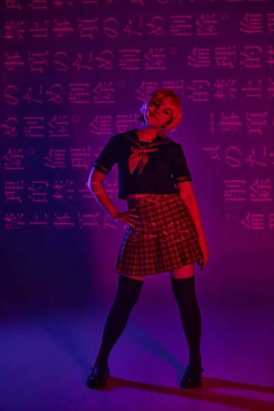 Anime donna in uniforme scolastica con mano sul fianco in luce al neon su sfondo viola con geroglifici — Foto stock