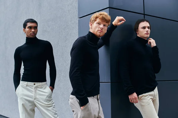 Trois beaux jeunes hommes en col roulé noir posant avec mur sur fond, concept de mode — Photo de stock