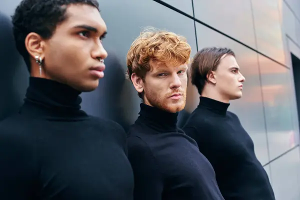 Hommes élégants multiethniques à col roulé posant épaule contre épaule debout par mur, concept de mode — Photo de stock