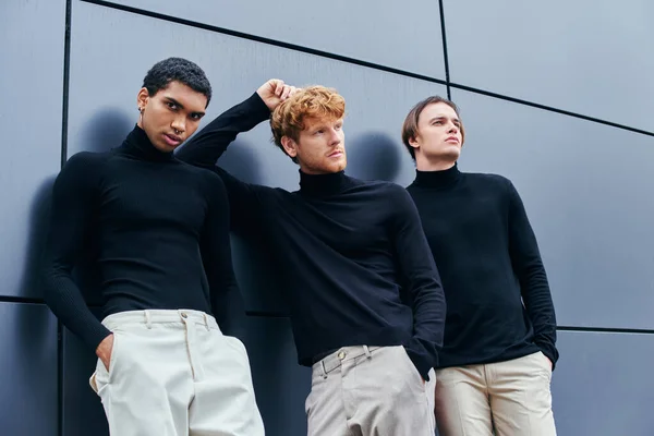 Red haired man posing with hand behind head among other men by wall, multicultural fashion shot — Stock Photo