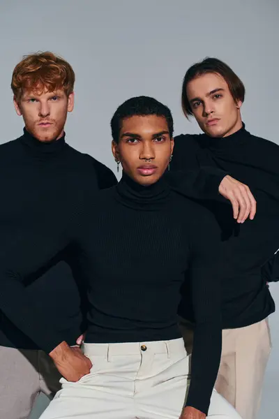 Tres hombres guapos interracial posando sobre fondo gris con cuellos altos, mirando a la cámara - foto de stock