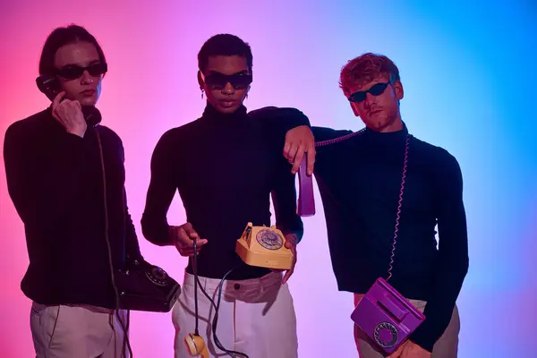 Tres hombres jóvenes con trajes negros que sostienen teléfonos fijos con gafas de sol, concepto de moda - foto de stock