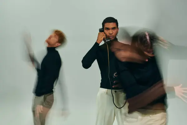 Joven afroamericano hombre posando con teléfono fijo con otros modelos masculinos en movimiento, larga exposición - foto de stock