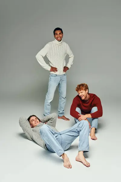 Tiro vertical de diversos amigos alegres en suéteres vibrantes posando sobre fondo gris, poder de los hombres - foto de stock