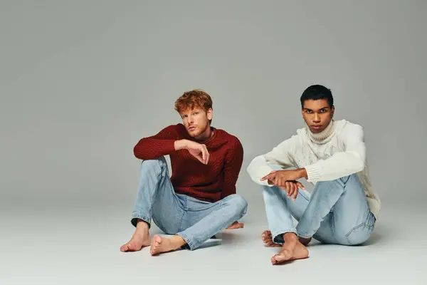 Multikulturell gut aussehende männliche Models in warmen Pullovern sitzen auf dem Boden und schauen in die Kamera, Männerpower — Stockfoto
