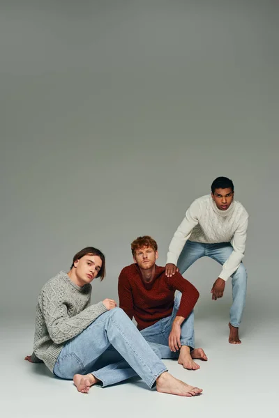 Interracial male models in vibrant sweaters posing on gray backdrop, hand on shoulder, men power — Stock Photo