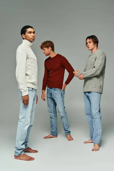 Atractivos hombres jóvenes en atuendo casual de pie quieto y posando sobre fondo gris, concepto de moda - foto de stock