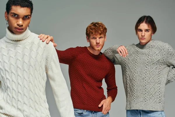 Good looking diverse men in sweaters with hands on each others shoulders looking at camera, fashion — Stock Photo