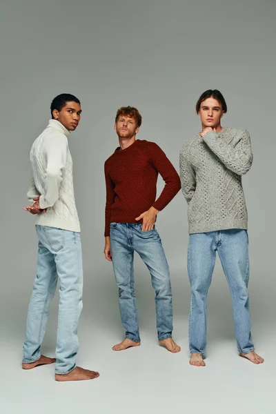 Vertical shot of young diverse friends in casual attires posing on gray backdrop, men power — Stock Photo