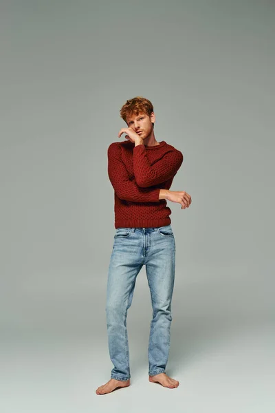 Гарний вигляд рудий волохатий чоловік теплий червоний светр і джинси позують рукою біля обличчя, концепція моди — стокове фото