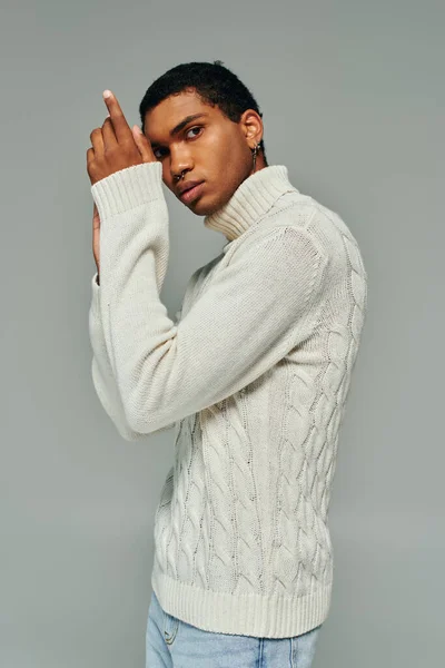 Atractivo hombre afroamericano en suéter blanco posando con las manos cerca de la cara mirando a la cámara - foto de stock