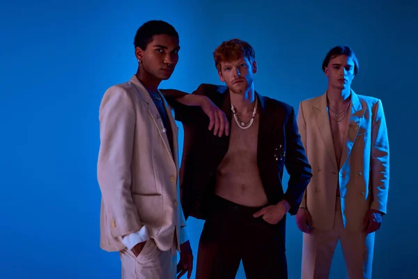 Three multicultural male models in vivid suits posing in neon lights, looking at camera, men power — Stock Photo