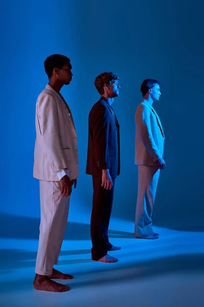 Tiro vertical de tres diversos hombres rodeados de luces de neón de pie en diagonal en una fila, poder de los hombres - foto de stock