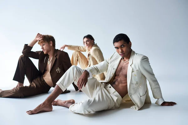 Bonito multicultural masculino modelos em ternos elegantes posando no chão com fundo cinza, homens poder — Fotografia de Stock