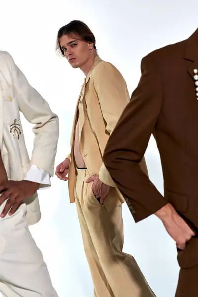 Focus on young man in unbuttoned suit posing next to other male models on gray backdrop — Stock Photo