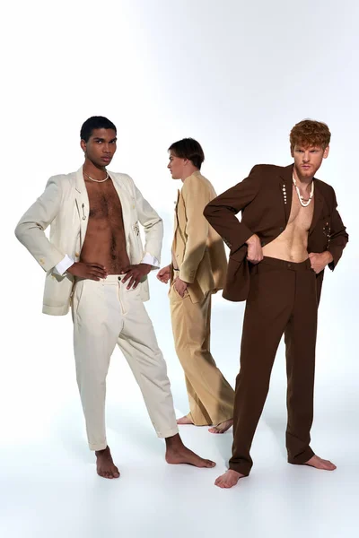Handsome multicultural trio in elegant suits standing on gray backdrop, gentlemen, men power — Stock Photo