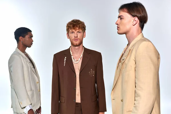 Two young men in stylish attires in profile with red haired man in unbuttoned suit looking at camera — Stock Photo