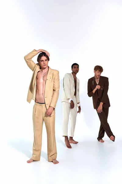 Tiro vertical de multiculturais jovens homens se movendo relaxadamente em trajes elegantes vívidos em pano de fundo branco — Fotografia de Stock