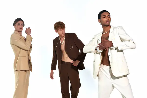 Привлекательное разнообразие трио в стильных расстегнутых костюмах, позирующих в движении на белом фоне, мужская сила — стоковое фото