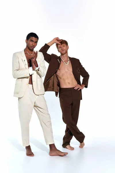 Vertical shot of multiethnic sexy men posing barefoot in suits on white backdrop, fashion concept — Stock Photo