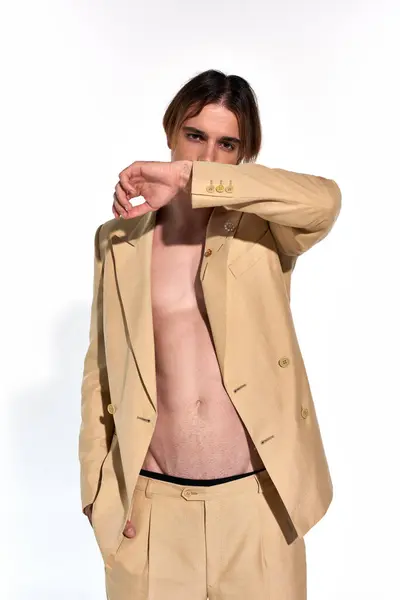 Hübsches junges männliches Model im knöpfchenlosen beigen Anzug mit erhobener Hand im Gesicht, Modekonzept — Stockfoto