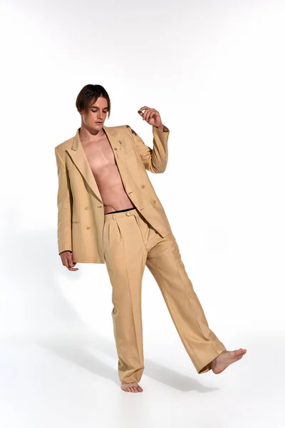 Vertical shot of sexy attractive man in unbuttoned beige suit posing in motion and looking down — Stock Photo