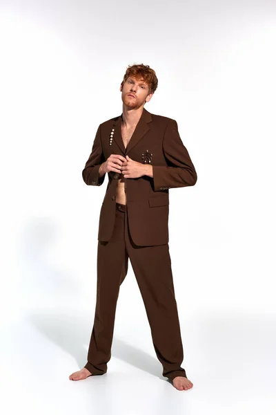 Vertical shot of appealing man with red hair and beard buttoning his elegant suit on white backdrop — Stock Photo