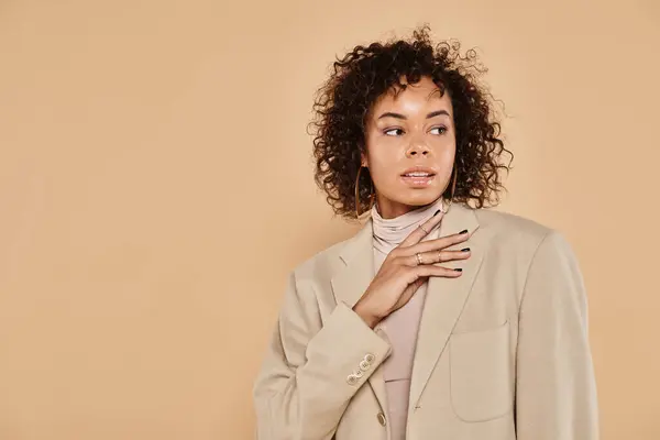 Brunette african american woman with curly hair posing in turtleneck and blazer on beige background — Stock Photo