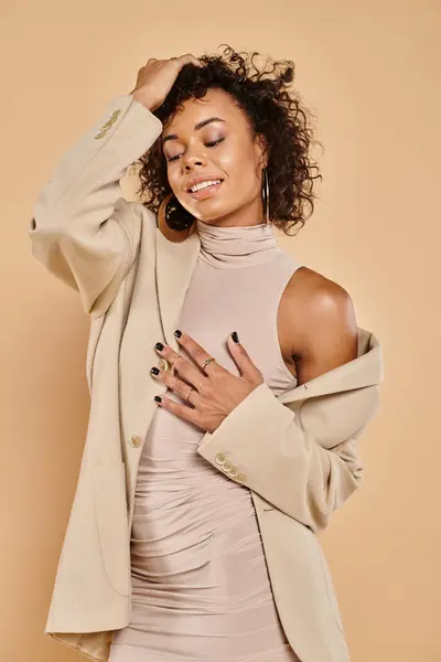 Joyful african american woman with curly brunette hair posing in autumnal attire on beige background — Stock Photo
