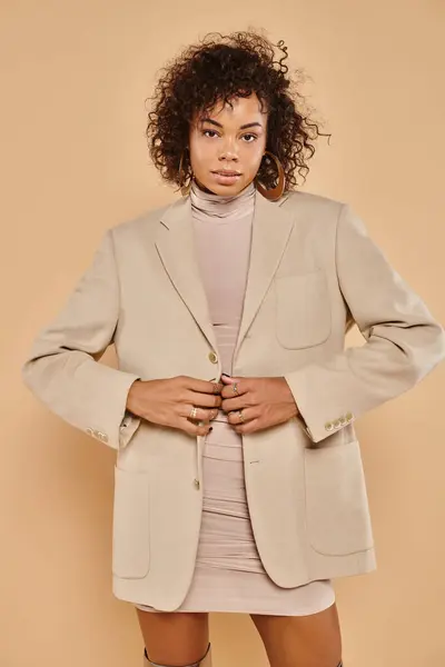 Autumn fashion, stylish african american woman posing in tight dress and blazer on beige backdrop — Stock Photo