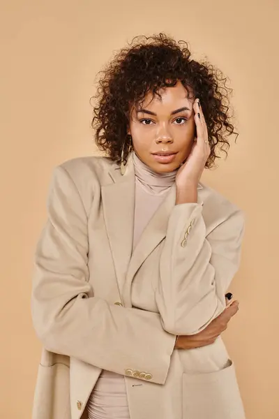 Moda de otoño, mujer afroamericana elegante posando en cuello alto y chaqueta sobre fondo beige - foto de stock