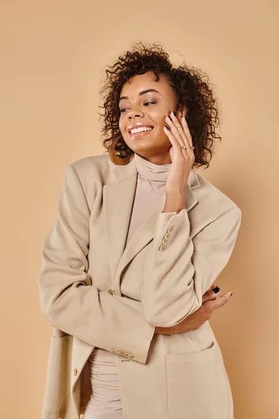 Autumn fashion, cheerful african american woman posing in turtleneck and blazer on beige backdrop — Stock Photo