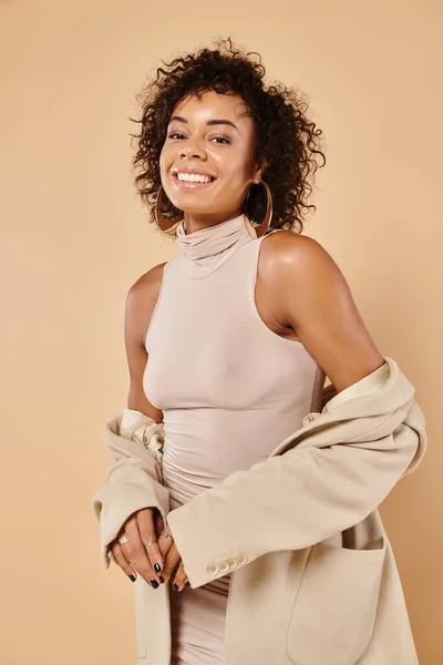 Autumn trends, pleased african american woman posing in blazer and tight dress on beige background — Stock Photo