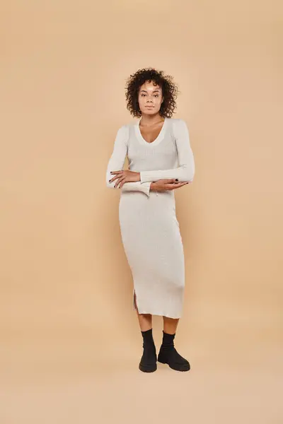 Brunette african american woman standing in midi dress and boots on beige backdrop, autumn style — Stock Photo