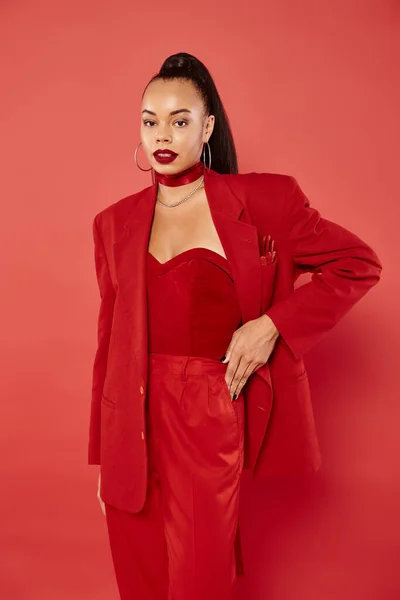 Bella donna afroamericana con coda di cavallo in posa in abito con mano sul fianco su sfondo rosso — Foto stock