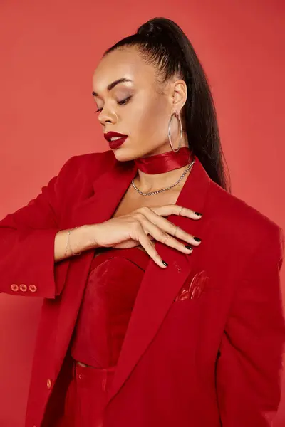 Elegante mujer afroamericana con cola de caballo de pelo liso posando en traje rojo y chaqueta conmovedora — Stock Photo